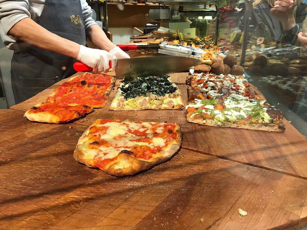 Assorted slices of Roman pizza al taglio with different toppings displayed at a pizza shop in Rome, Italy.