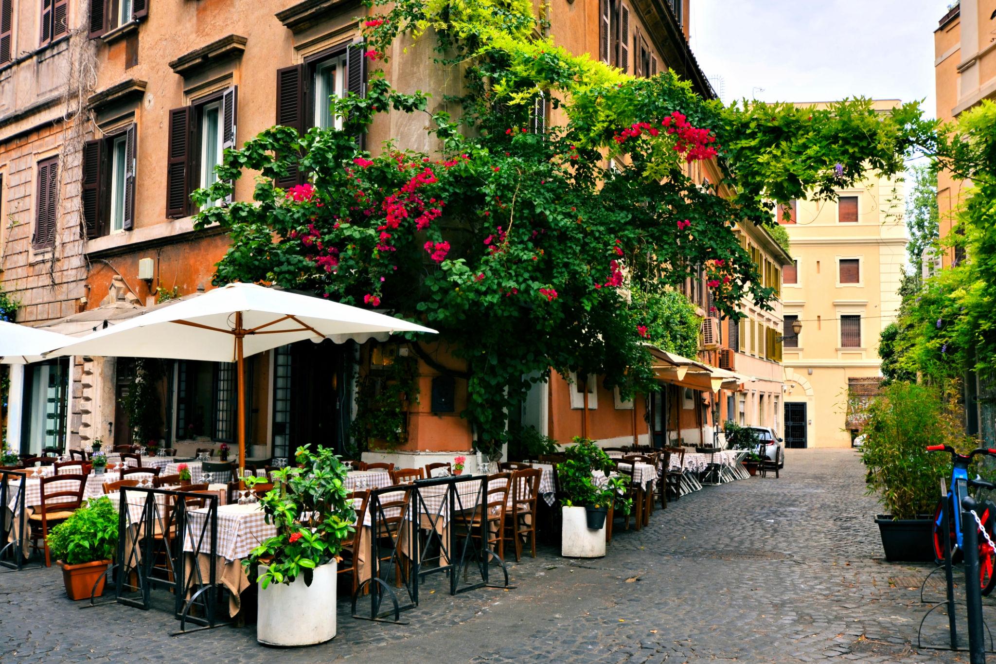 Outdoor café seating along a charming street in Rome, Italy, with historic buildings and greenery.