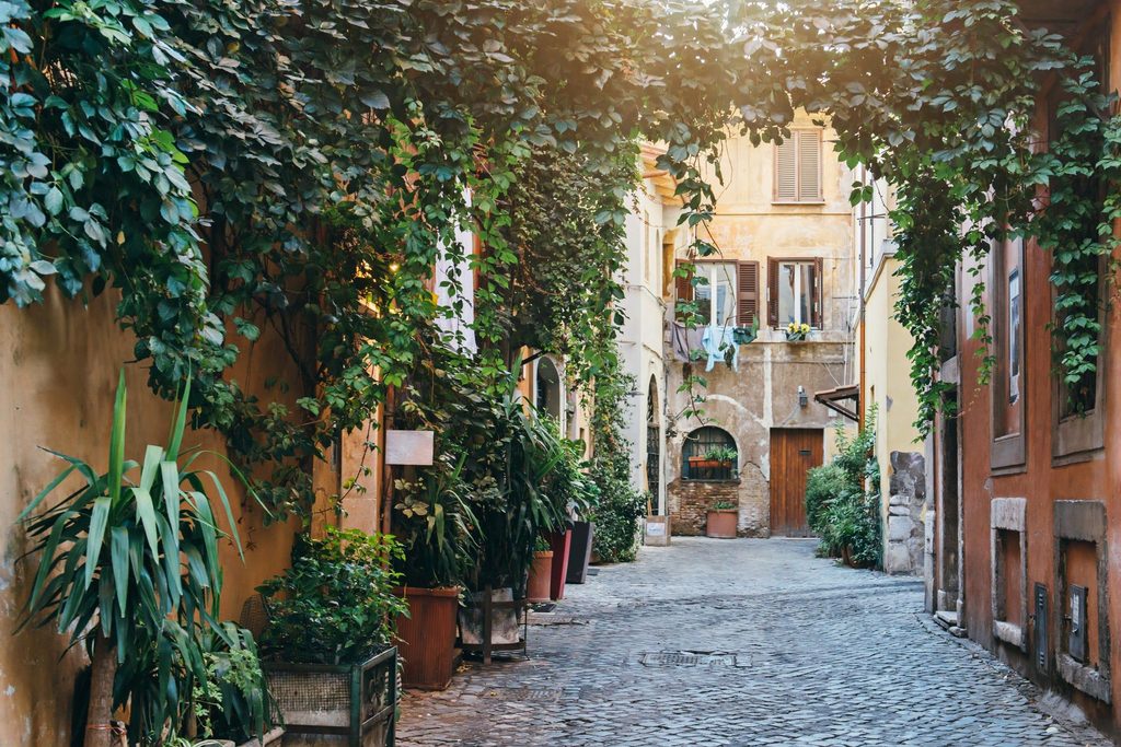 Quiet cobblestone street in Trastevere, Rome, lined with historic Italian buildings, colorful facades and greenery.