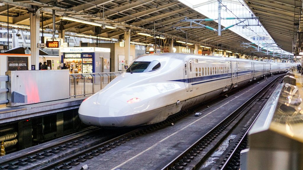 White and blue Shinkansen bullet train standing at a Japanese railway station platform, illustrating high-speed rail travel between Tokyo, Kyoto, and Osaka.