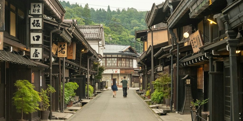 Traditional wooden merchant houses lining a quiet historic street in Takayama Old Town, Japan, with Japanese shop signs and visitors walking along the street.